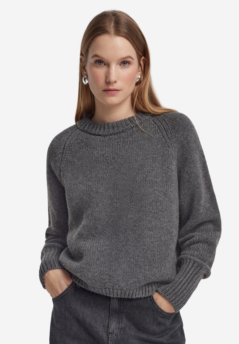 Maglione grigio in maglia con scollo rotondo a coste e maniche lunghe, caratterizzato da una vestibilità rilassata e una texture sottile. Abbinato a jeans scuri.