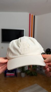 Hvit baseballcaps i bomull med en strukturert overflate, med et sydd bokstav "B" på forsiden og en buet brem.