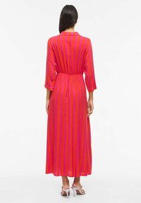 Robe longue et fluide avec des rayures verticales roses et violettes, dotée d'un col, d'une ceinture élastique et de manches trois-quarts. Texture de tissu douce.