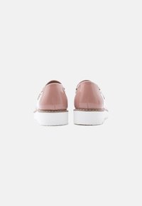 Paire de chaussures à plateforme roses brillantes avec semelles épaisses blanches, vues de dos sur un fond clair uni.