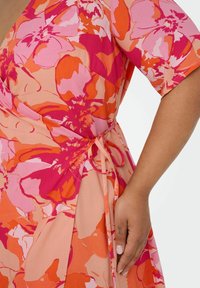 Floral wrap dress in orange and pink hues. Lightweight fabric with short sleeves, featuring a tie at the waist and soft floral patterns.
