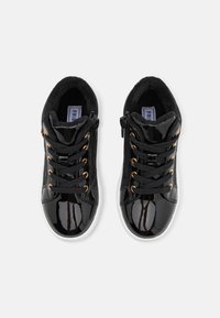Zapatillas de charol negro con forro de pelo sintético, ojales dorados y cordones negros. Con cremallera lateral y suelas de goma blanca.
