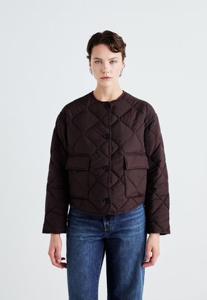 Veste matelassée marron avec un col rond, fermeture à boutons sur le devant et deux poches plates. Portée sur un jean en denim bleu.