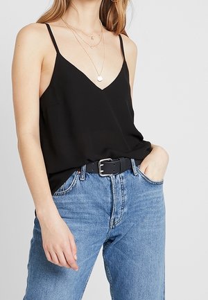 Top nero senza maniche con scollatura a V, abbinato a jeans a vita alta azzurri e una cintura nera con fibbia.