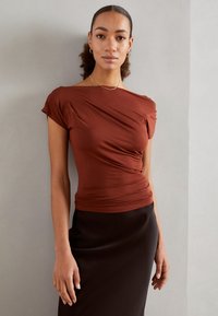 Rustfarget topp med draperingsdesign, korte ermer og en tettsittende silhuett, kombinert med et elegant svart skjørt. Glatt, mykt stoff.