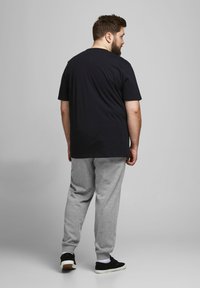 Camiseta de algodón negra, pantalones de chándal grises y zapatillas negras. El atuendo tiene un corte relajado y se muestra desde la parte posterior.