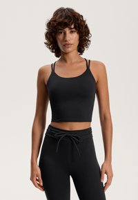 Čierny skrátený top bez rukávov s tenkými nastaviteľnými ramienkami a hladkou, elastickou textúrou, kombinovaný s čiernymi nohavicami s vysokým pásom a s možnosťou stiahnutia pomocou šnúrky.