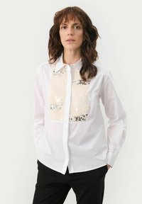White button-up shirt with a sequin-embellished front panel in cream and silver tones; features a classic collar and long sleeves.