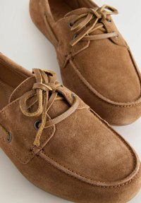 Bruine suède schoenen met veters hebben metallic oogjes, een ronde neus en contrasterende stiksels. Zachte textuur met een casual ontwerp.
