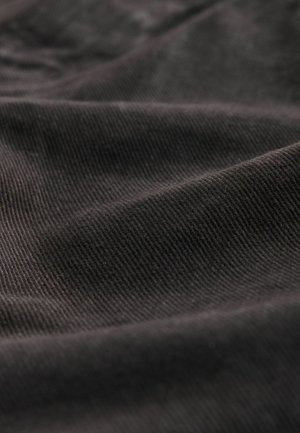 Schwarzer Cord-Stoff mit feinen Rippungen, der eine weiche Textur und einen subtilen Glanz zeigt und in sanften Falten arrangiert ist.