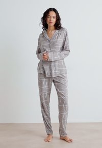 Pajamas gris clair en tissu lisse, présentant un motif abstrait blanc. L'ensemble comprend une chemise à boutons et un pantalon assorti.