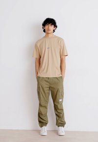 Tan bomulds t-shirt med et lille logo, parret med olivengrønne cargobukser med sidelommer og hvide sneakers.