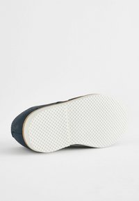 Sneaker en cuir bleu marine avec une semelle en caoutchouc blanc texturé, présentant une forme arrondie et un design minimaliste. Coutures renforcées visibles sur les bords.