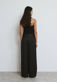 Top negro sin tirantes combinado con pantalones de pierna ancha de rayas con un acabado texturizado. Modelo visto desde atrás.