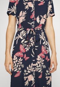 Abito floreale in tessuto blu navy con motivi di farfalle rosa e rosse, maniche corte, abbottonatura frontale e una cintura annodata per un tocco di stile.