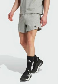 Pantalones cortos deportivos grises con aberturas laterales, hechos de tela ligera, combinados con calcetines deportivos negros y zapatos con un logo blanco.