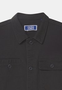 Black button-up shirt with a classic collar, two front pockets, and a fabric label. Features black buttons and a smooth texture.