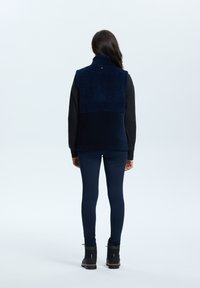 Marineblauer Fleece-Weste mit hohem Kragen, strukturiertem oberen Bereich und glattem unteren Bereich, getragen über einem schwarzen Langarmshirt und Leggings.