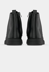 Stivaletti neri alla caviglia con una finitura in pelle liscia, chiusura con zip sul retro e suole in gomma robuste. Design minimalista con una silhouette snella.