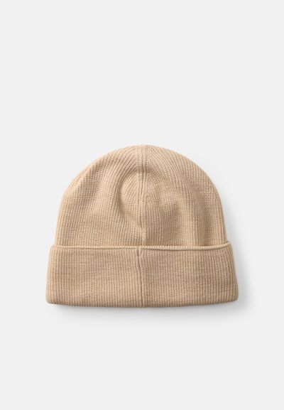 Gorro de punto beige con un dobladillo. La tela texturizada muestra un sutil acanalado. Parte superior redondeada sin patrones ni adornos.