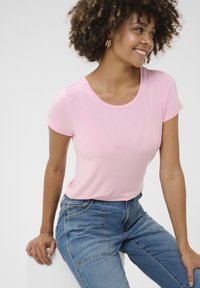 Camiseta de manga corta rosa claro con escote redondo, hecha de tela suave. Combinada con jeans azules de tiro alto, que cuentan con bolsillos delanteros.
