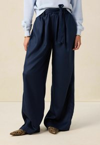 Marineblauwe wijde broek van soepel materiaal, met een knooptaille en een vloeiende silhouet. Dragen met slangenprintpuntige flats.