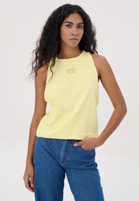 Geel mouwloos crop top met een ronde halslijn, voorzien van subtiele logo-details. Gepaard met hoge taille blauwe denim jeans.