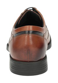 Bruine leren herenschoen met zwarte zool, zichtbare stiksels en een zwarte strook bij de hak, weergegeven vanaf de achterkant.