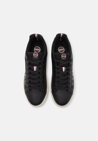 Svarta lädersneakers med vita gummisålar, med platta snören, runda logotags och ett texturerat mönster på sidan i en elegant design.