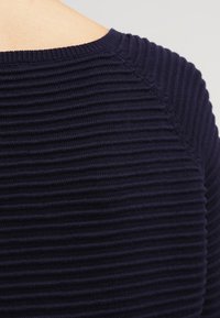 Maglione a coste blu navy scuro con collo rotondo e tessuto strutturato, che mette in evidenza il motivo costante e la sagomatura lungo le spalle.