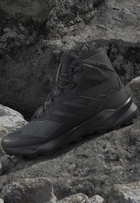 Black high-top hiking shoe with mesh and synthetic upper, rugged sole, and pull tab, placed on rough rocky surface.