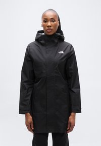 Μαύρο αδιάβροχο μπουφάν με κουκούλα, με φερμουάρ μπροστά, μακριά μανίκια και λογότυπο στο στήθος. Λείο, ελαφρύ υλικό.