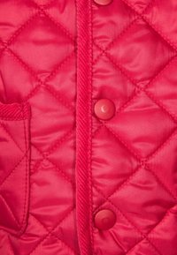 Červená prošívaná bunda s diamantovým vzorem, kulatými knoflíky, malou kapsou a hladkým, lesklým texturovaným materiálem.