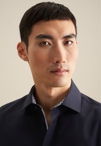 Marineblauwe button-up shirt met een kraag en een gepatterneerde binnenkant. Soepele textuur, slim fit ontwerp en contrasterende details op de kraag.