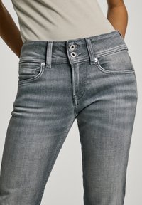 Šedé džínové kalhoty s úzkým střihem, vybavené dvojitým zapínáním, pěti kapsami a jemným šisováním na stehnech.