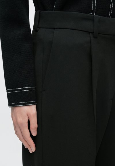 Fekete, szabott nadrágok redőzött kialakítással, sima szövetes felülettel és a derékrészen hozzáillő övhurkokkal kiemelve.