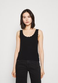 Sort ribbet tanktop med scalloped halsudskæring og brede stropper, med en tætsiddende pasform og blød tekstur. Passer godt til sorte højtaljede jeans.