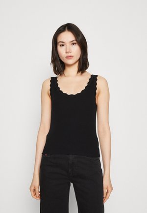 Débardeur noir à côtes avec un col festonné et des bretelles larges, présentant une coupe ajustée et une texture douce. Se marie avec un jean noir taille haute.