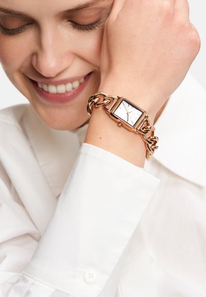Rose gold watch featuring a rectangular face with a white dial, chain link bracelet, and minimalist hour markers. Worn on a wrist.