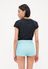 Schwarzes kurzärmeliges Oberteil mit glatter Textur, kombiniert mit hellblauen, gerippten Shorts mit einem breiten Bund.