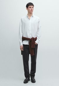 Camicia bianca abbottonata, pantaloni scuri e scarpe nere. Maglione marrone a maglia legato in vita. Tessuto liscio e vestibilità comoda.