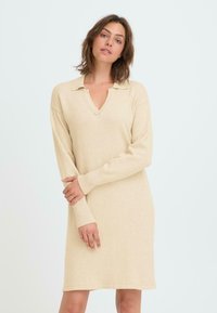 Vestito beige lavorato a maglia con colletto, scollatura a V, maniche lunghe e polsi a coste. Tessuto morbido e vestibilità dritta, che arriva sopra il ginocchio.