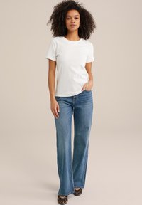 Witte t-shirt met korte mouwen, gecombineerd met lichtblauwe flared jeans, met een ontspannen pasvorm en een licht beschadigde textuur. Dierlijke print schoenen inbegrepen.