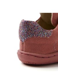 Chaussure en suede rose avec un capuchon de talon en paillettes scintillantes, affichant des coutures visibles et une semelle texturée. Design compact adapté pour un usage décontracté.