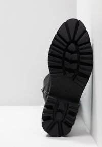 Chaussures noires avec une semelle en caoutchouc texturée comprenant des crampons profonds et un talon renforcé. La tige est faite d'un matériau en tissu lisse.