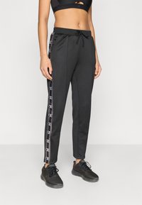 Μαύρο αθλητικό παντελόνι με στενή εφαρμογή, διαθέτει κορδόνι στη μέση και πλευρικές λεπτομέρειες σε αντίθετο μοτίβο. Φοριέται με μαύρα αθλητικά παπούτσια.