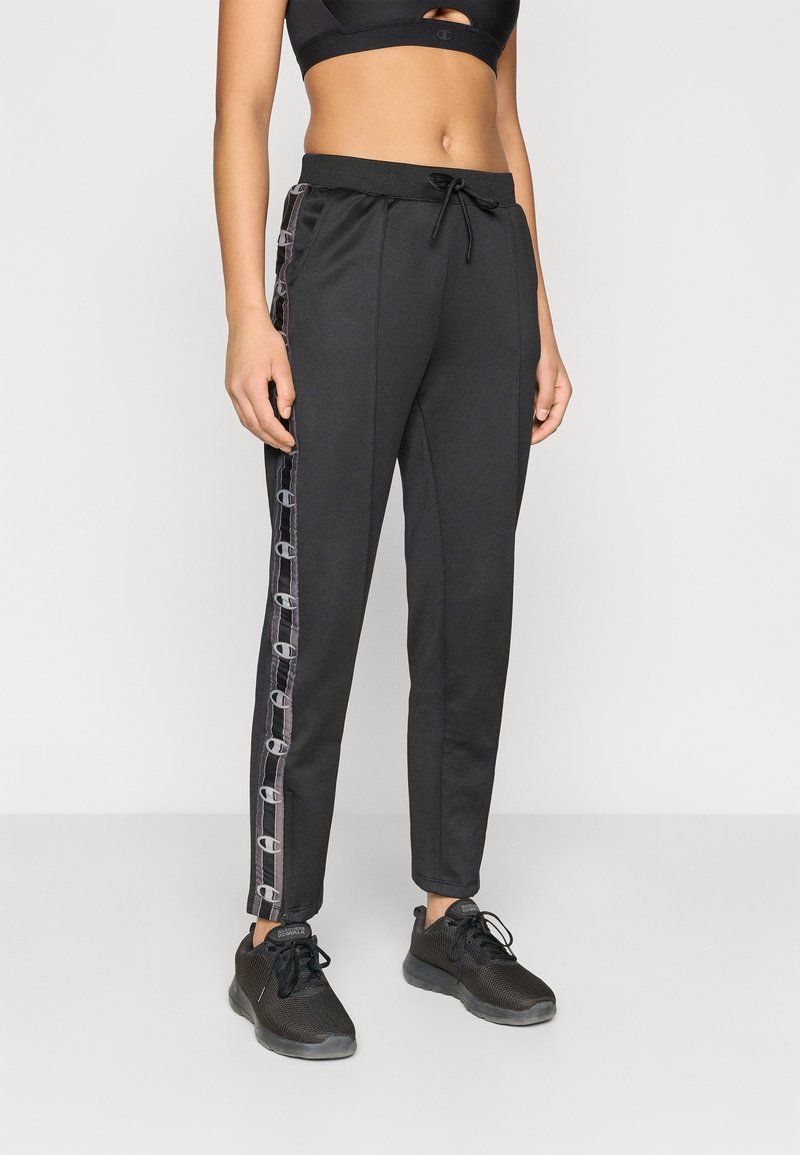 Μαύρο αθλητικό παντελόνι με στενή εφαρμογή, διαθέτει κορδόνι στη μέση και πλευρικές λεπτομέρειες σε αντίθετο μοτίβο. Φοριέται με μαύρα αθλητικά παπούτσια.