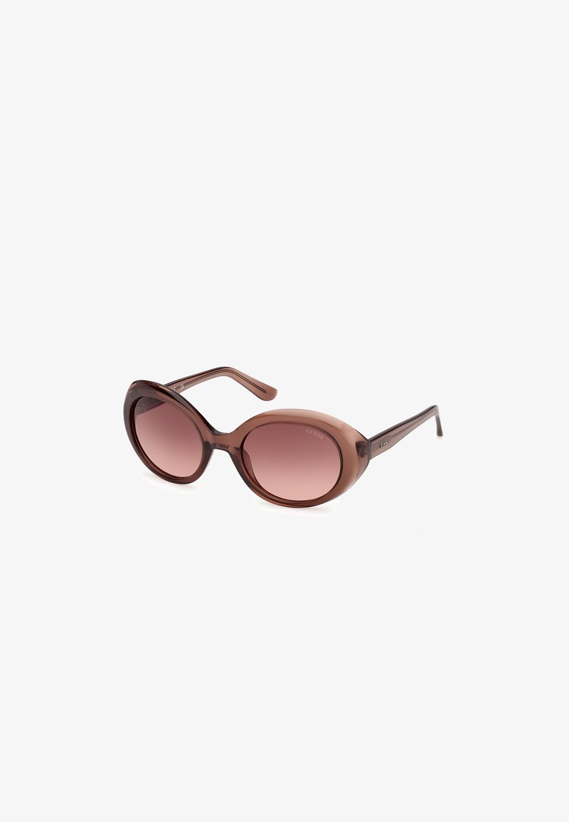 Lunettes de soleil en plastique transparent marron de forme ovale avec des verres dégradés marron et des branches incurvées.