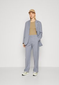 Lichtblauw op maat gemaakt pak met een beige top, aangevuld met een beige pet en witte sneakers met gele accenten. Gladde stof, elegante silhouet.