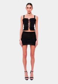 Black cropped top with lace-up front, ruffled edges; matching black mini skirt. Model wears black high-heeled sandals. Clean design.